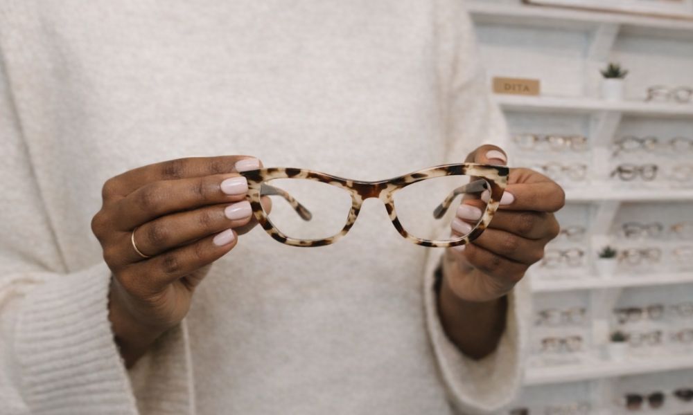 A woman putting on a pair of tortoiseshell glasses